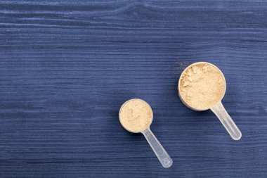 Scoops filled with protein powders on background blue wood clipart