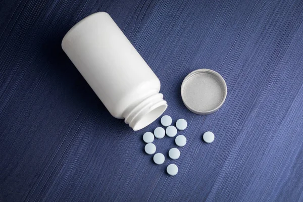 Blue pills spilling out of pill bottle and blue wood background. Top view with copy space. Medicine concept