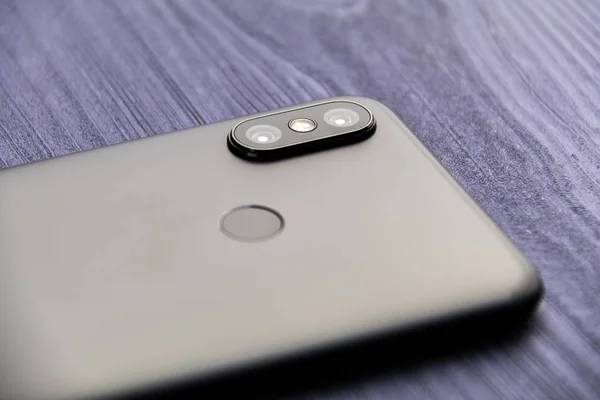 İki kamera ve parmak izi okuyucusu olan siyah bir akıllı telefon. Çift kameralı akıllı telefon mavi ahşap masada yakın