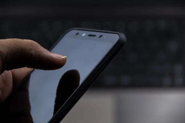Mão usando um celular moderno e um laptop de fundo — Fotografia de Stock