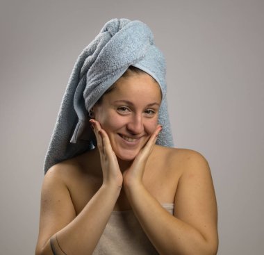 Duştan sonra havluyla mutlu bir genç kadın. Yüzüne dokunuyor.