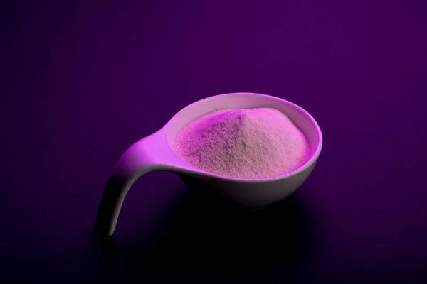 Whey protein powder sports bodybuilding supplement. Top view white porcelain scoop with vanilla flavor powder. Black background and purple light