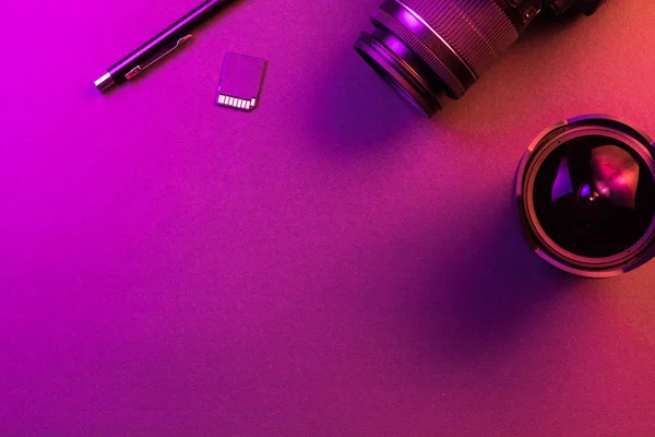 Macchina fotografica, matita, lente di occhio di pesce e scheda SD. Luce rosa. Vista dall'alto dello spazio di lavoro. Copia spazio — Foto Stock