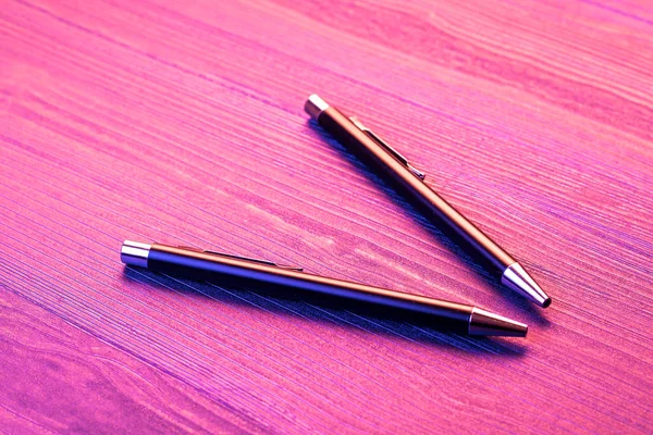 Dos bolígrafos elegantes sobre fondo de madera y luz rosa. Negocio negro pluma . — Foto de Stock