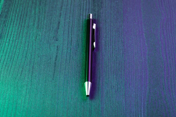 Elegant pen on wood background and green and blue light. Business black pen. Top view