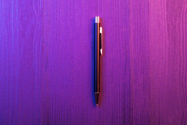 Елегантна ручка на фоні дерева, фіолетове і рожеве світло. Бізнес чорна ручка. Вид зверху — стокове фото