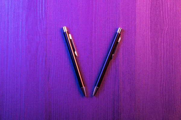 Two elegant pen on wood background and pink and blue light. Business black pen. Top view