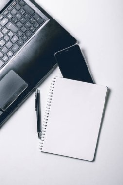 Dizüstü bilgisayar, akıllı telefon ve diğer malzemeleri ile modern beyaz ofis masası masa. Ortadaki metni giriş için boş not defteri sayfası. Üst görünüm, düz yatıyordu.