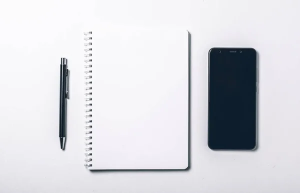 带笔和智能手机的现代白色办公桌桌。空白笔记本页，用于在中间输入文本。顶视图，平铺. — 图库照片