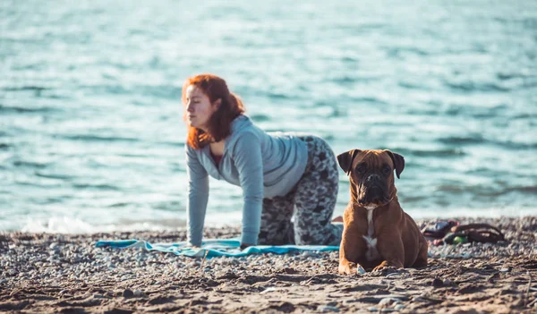 Młoda kobieta uprawia jogę i rozciąga się na plaży ze swoim psem — Zdjęcie stockowe