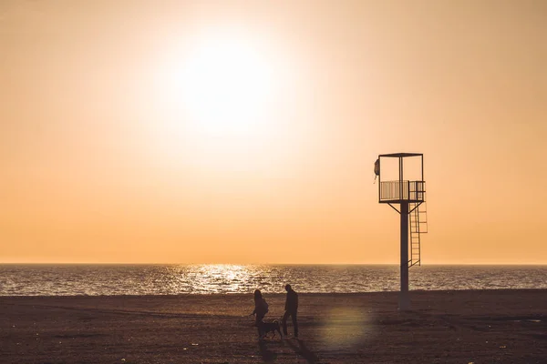 Casal passeando ao longo de uma praia deserta ao pôr do sol — Fotografia de Stock
