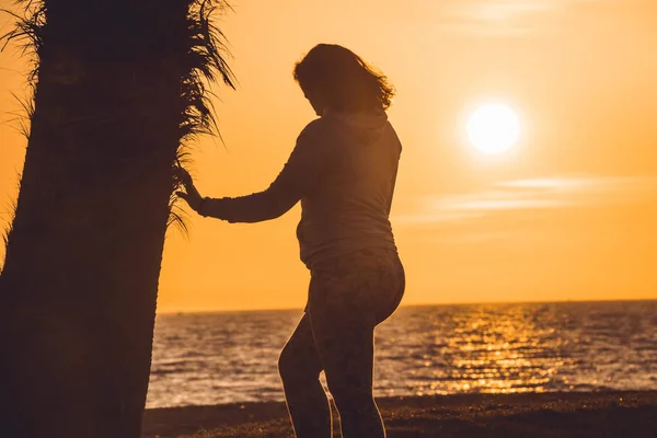 Mulher grávida tocando sua barriga e observando o pôr do sol, ao lado de uma palmeira, em Almerimar, Almeria, Espanha — Fotografia de Stock