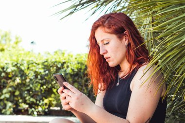 Parkta oturan bir akıllı telefon medya izlerken Mutlu kız