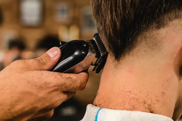 Молодой красавчик-парикмахер стрижет подростка в парикмахерской — стоковое фото