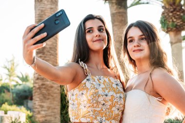 Lezbiyen bir çift ağaçların arkasında yan yana durup selfie çekiyor.