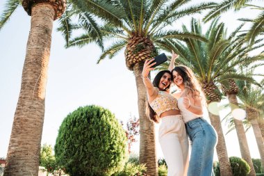 Lezbiyen bir çift ağaçların arkasında yan yana durup selfie çekiyor.