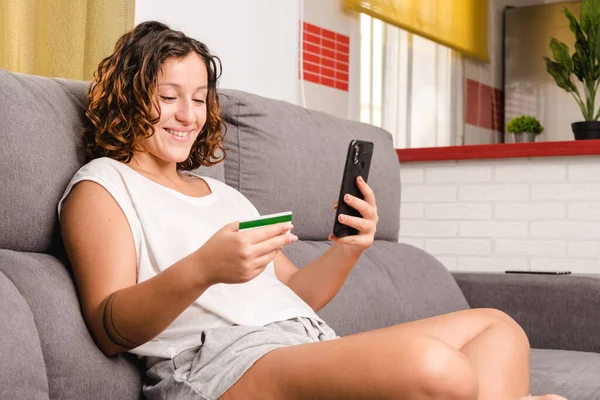 Frau auf der Wohnzimmercouch kauft online mit Kreditkarte und Smartphone ein — Stockfoto