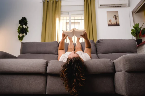 Frau liest im Wohnzimmer ein Buch und sitzt auf der Couch — Stockfoto