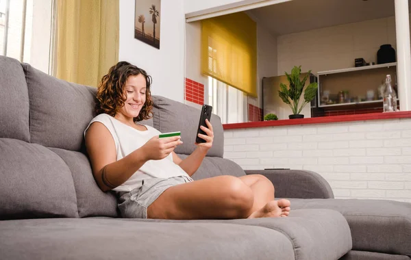 Frau auf der Wohnzimmercouch kauft online mit Kreditkarte und Smartphone ein — Stockfoto