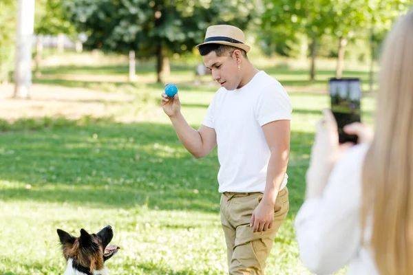 Młody Latynos bawi się i trenuje ze swoim granicznym psem collie, podczas gdy jego dziewczyna robi mu zdjęcie komórką — Zdjęcie stockowe