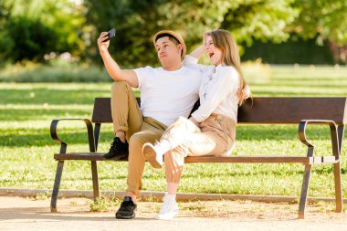 Parkta cep telefonlarından selfie çeken genç bir çift. Latin erkek ve beyaz kadın.