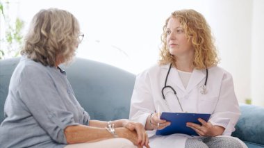 Doktor elinde not panosu ev ziyareti sırasında sağlık durumu hakkında yaşlı kadına danışıyor.