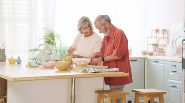 Mutlu emekli çift, modern mutfaklarında birlikte sağlıklı bir yemek hazırlıyor, zamanlarının tadını çıkarıyor ve sağlıklı bir yaşam tarzı geliştiriyorlar.
