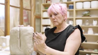 Pembe saçlı, ıslak balçığı şekillendiren, çanak çömlek çarkında çalışan, yaratıcı atölye atölyesinde seramik işçilik sergileyen kadın bir zanaatkar.