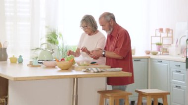 Modern mutfakta işbirliği yapan emekli yaşlılar taze salata hazırlıyor ve renkli sebzeleri birlikte doğrarken kaliteli zaman geçiriyorlar.