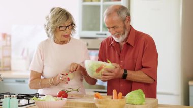 Yaşlı bir çift mutfakta salata tatlandırıyor, baharat ekliyor ve birlikte vakit geçiriyorlar.