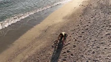 Deneyimli kadın fitness eğitmeni kayalık çakıl taşı sahil şeridinde sakin gündoğumu meditasyonu sırasında ustrasana yoga pozu değişimi sergiliyor.