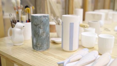 Bir çömlek atölyesinde ahşap bir masada sergilenen zarif seramik vazolar, araçlar ve diğer eserlerle çevrili.