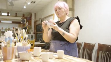 Profesyonel seramistim küçük seramik kaseyi düzeltiyor, titiz işçilik ve şahsi atölye atölyesinde zanaatkarlık sergiliyor.