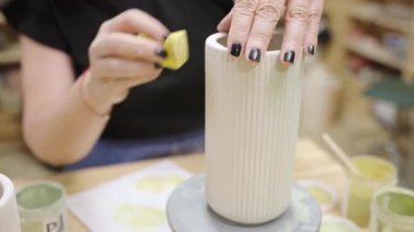 Beyaz flütlü seramik vazonun üzerine yeşil pigment boyayan yetenekli kadın seramikçi, zanaatkar çömlek atölyesindeki karmaşık el sanatları çalışmalarını vurguluyor.