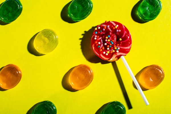 a Lollipop on a stick lies among a pattern of colored candies on a bright yellow background