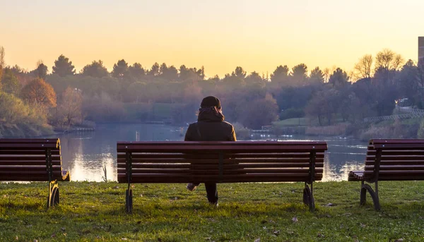 man sitting on bench in park and looking at lake