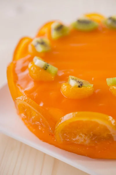 orange cake decorated with kiwi fruit and slices of oranges on white plate