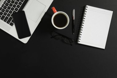 Dizüstü bilgisayar, akıllı telefon, defter, gözlük ve kahve siyah arka plan üzerine.