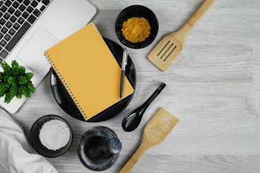 Çatal bıçak takımı baharatlar, chilies, harç, laptop ve defter ile ahşap masa arka plan ayarla. Mutfak gereçleri.