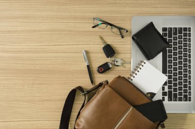 Erkek deri çanta kişisel eşyaları ve ahşap masa laptop ile.