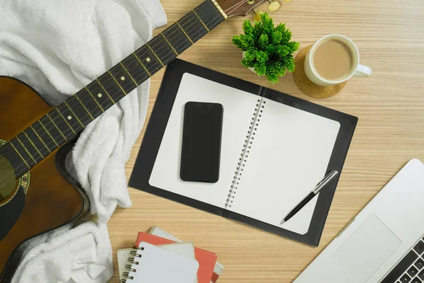 Akustik gitar, defter, akıllı telefon ve diğer birden çok öğe üzerinde ahşap arka plan. Natürmort düz lay.