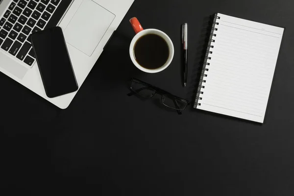 Dizüstü bilgisayar, akıllı telefon, defter, gözlük ve kahve siyah arka plan üzerine.