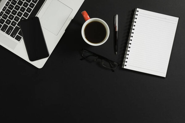 Laptop, smart phone, notebook, eyeglasses and coffee on black background.