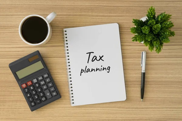 Vergi planlaması defter üzerinde yazılı. Office ile ahşap masa üstten görünüm kaynağı.