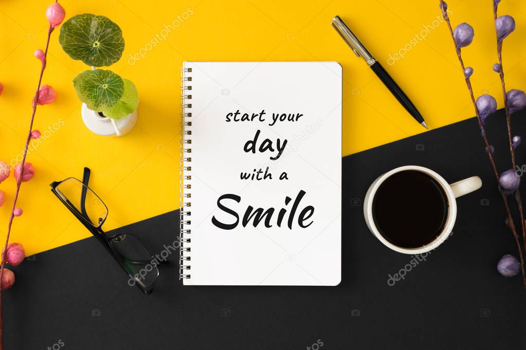 Notebook with motivational and inspirational wisdom quote on yellow and black background. Start your day with a smile.
