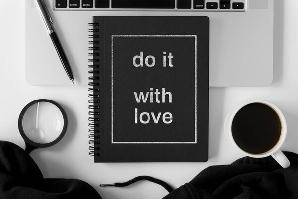 Notebook with wisdom quote and laptop on white office table.