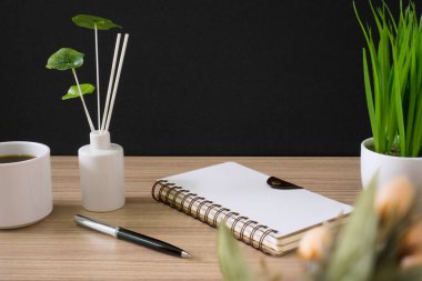 Spiral defter ile kahve fincanı ve siyah arka plan ile ahşap masa üzerinde Saksı bitki.