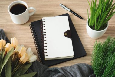Spiral defter ile kahve fincanı ve çiçek ahşap masa.