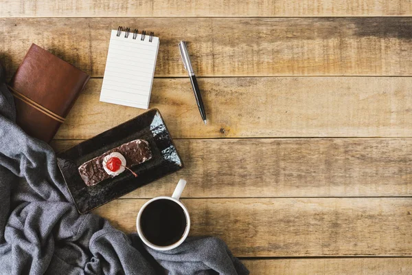 Small spiral notepad, butterscotch cake and cup of coffee on rustic wood. Flat lay.