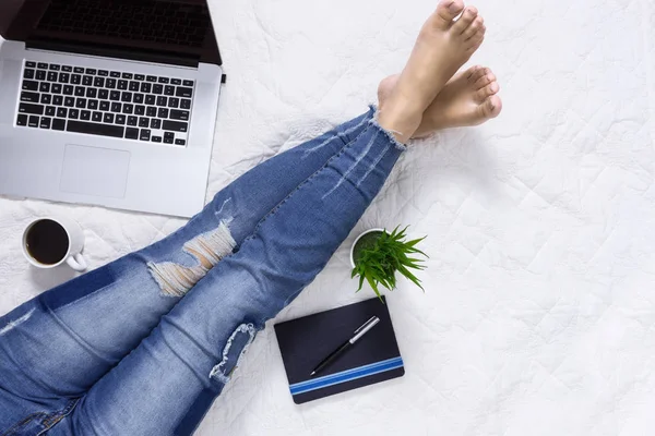 Yatağın üstüne oturan ve laptop ile çalışma denim kot giyen kadın. Aile içi yaşam yaşam tarzı kavramı.